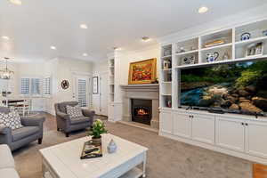 Living room featuring ornamental molding, a warm lit fireplace, built in shelves, and recessed lighting
