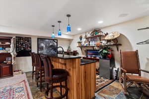 Indoor wet bar with dark stone finish flooring, freestanding refrigerator, dark stone countertops, pendant lighting, and wood finish cabinets