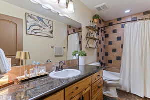 Full bathroom featuring vanity, shower / tub combo with curtain, and dark stone finish floors