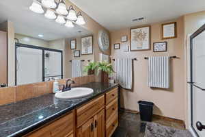 Full bathroom with a shower stall, vanity, and dark stone finish flooring