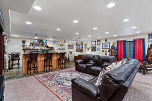 Living room with a dry bar, recessed lighting, and dark stone finish floors
