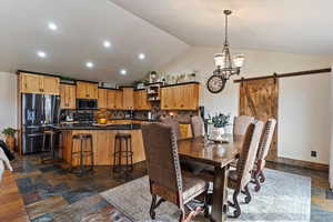 Dining space with a barn door, hanging lights, stone tile floors, and lofted ceiling