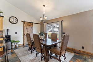 Dining space featuring stone tile flooring, a barn door, lofted ceiling, and hanging lights