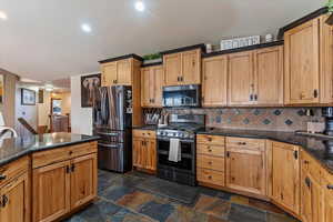 Kitchen featuring stainless steel appliances, decorative backsplash, dark stone counters, stone tile floors, and recessed lighting