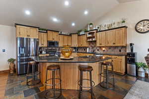 Kitchen featuring stainless steel appliances, backsplash, dark stone counters, vaulted ceiling, and a kitchen island