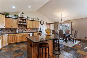 Kitchen with a center island, dark stone counters, open shelves, suspended lighting, and decorative backsplash