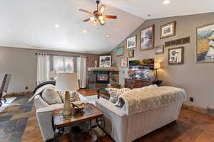Living area with a ceiling fan, a stone fireplace, recessed lighting, and vaulted ceiling