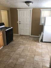 Kitchen featuring black range with gas cooktop, freestanding refrigerator, and a textured ceiling