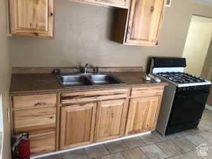Kitchen featuring black gas range oven, light wood finish cabinetry, dark countertops, and light tile patterned floors