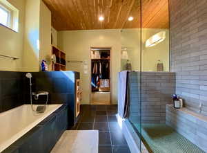 Full bathroom featuring dark tile patterned flooring, a garden tub, a walk in shower, wooden ceiling, and a walk in closet