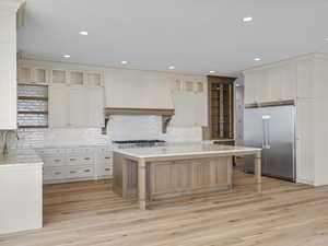 Two tone kitchen featuring built in fridge, a center island, light wood-type flooring, a breakfast bar area, and recessed lighting