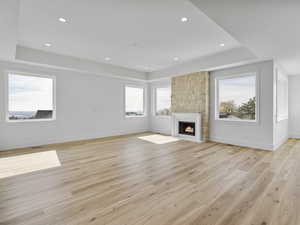 Unfurnished living room featuring a fireplace, a raised ceiling, light wood-style floors, and recessed lighting