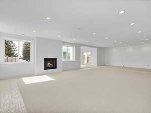 Unfurnished living room featuring a glass covered fireplace, light colored carpet, and recessed lighting