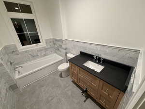 Full bathroom with vanity, wainscoting, a bath, and tile walls