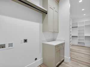 Laundry area with hookup for an electric dryer, light wood finished floors, recessed lighting, cabinet space, and washer hookup