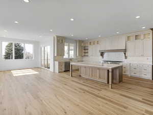 Kitchen featuring glass fronted cabinets, open floor plan, a center island, light wood finished floors, and backsplash
