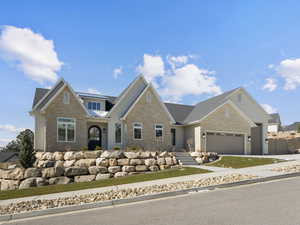 Craftsman-style home featuring a garage, a shingled roof, stone siding, and driveway