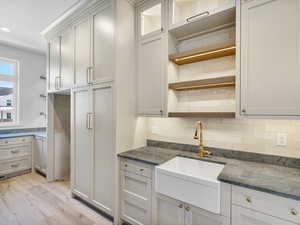 Kitchen with open shelves, light wood-style flooring, backsplash, white cabinets, and dark stone countertops