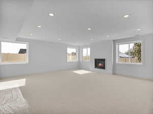 Unfurnished living room featuring a glass covered fireplace, healthy amount of natural light, carpet flooring, and recessed lighting