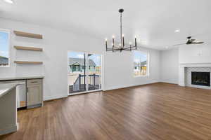 Unfurnished living room featuring ceiling fan, dark wood finished floors, a fireplace, and hanging lights