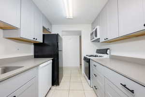 Kitchen with white appliances, light tile patterned floors, white cabinets, and a textured ceiling