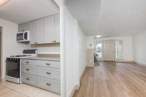Kitchen featuring gas stove, light countertops, a textured ceiling, white microwave, and light wood finished floors