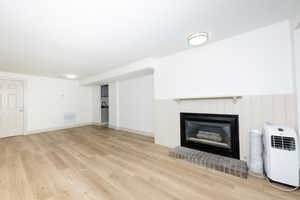 Unfurnished living room with light wood-type flooring, a fireplace, and a wainscoted wall