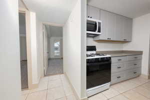 Kitchen with gas range oven, white microwave, a textured ceiling, light tile patterned floors, and light countertops