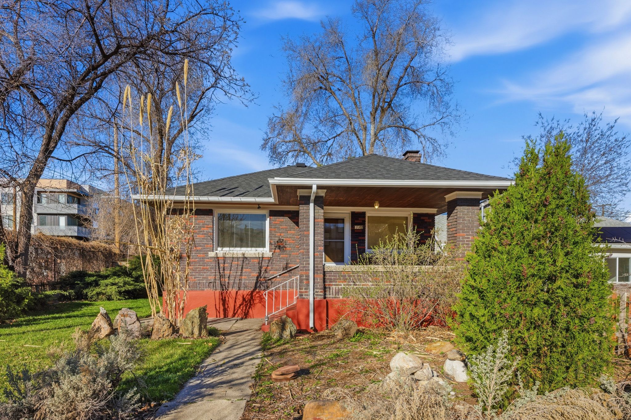 View of front of house featuring a porch, brick siding, a chimney, and roof with shingles