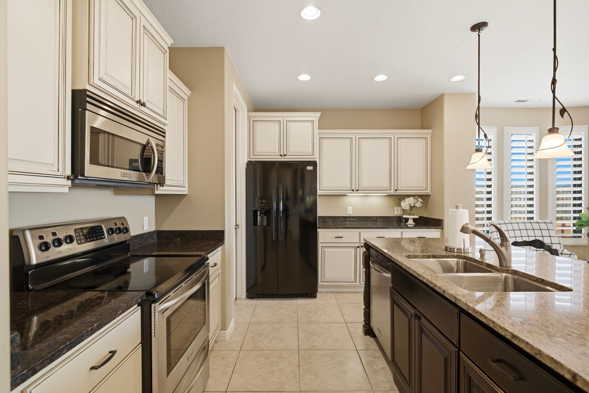 Kitchen with stainless steel appliances, pendant lighting, dark stone counters, two tone color scheme, and light tile patterned floors