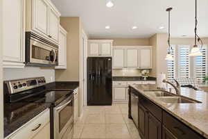 Kitchen with stainless steel appliances, pendant lighting, dark stone counters, two tone color scheme, and light tile patterned floors