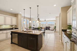 Kitchen featuring two tone color scheme, open floor plan, dark stone countertops, a kitchen island with sink, and decorative light fixtures