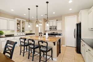 Kitchen featuring a breakfast bar area, stainless steel appliances, an island with sink, white cabinets, and light tile patterned flooring