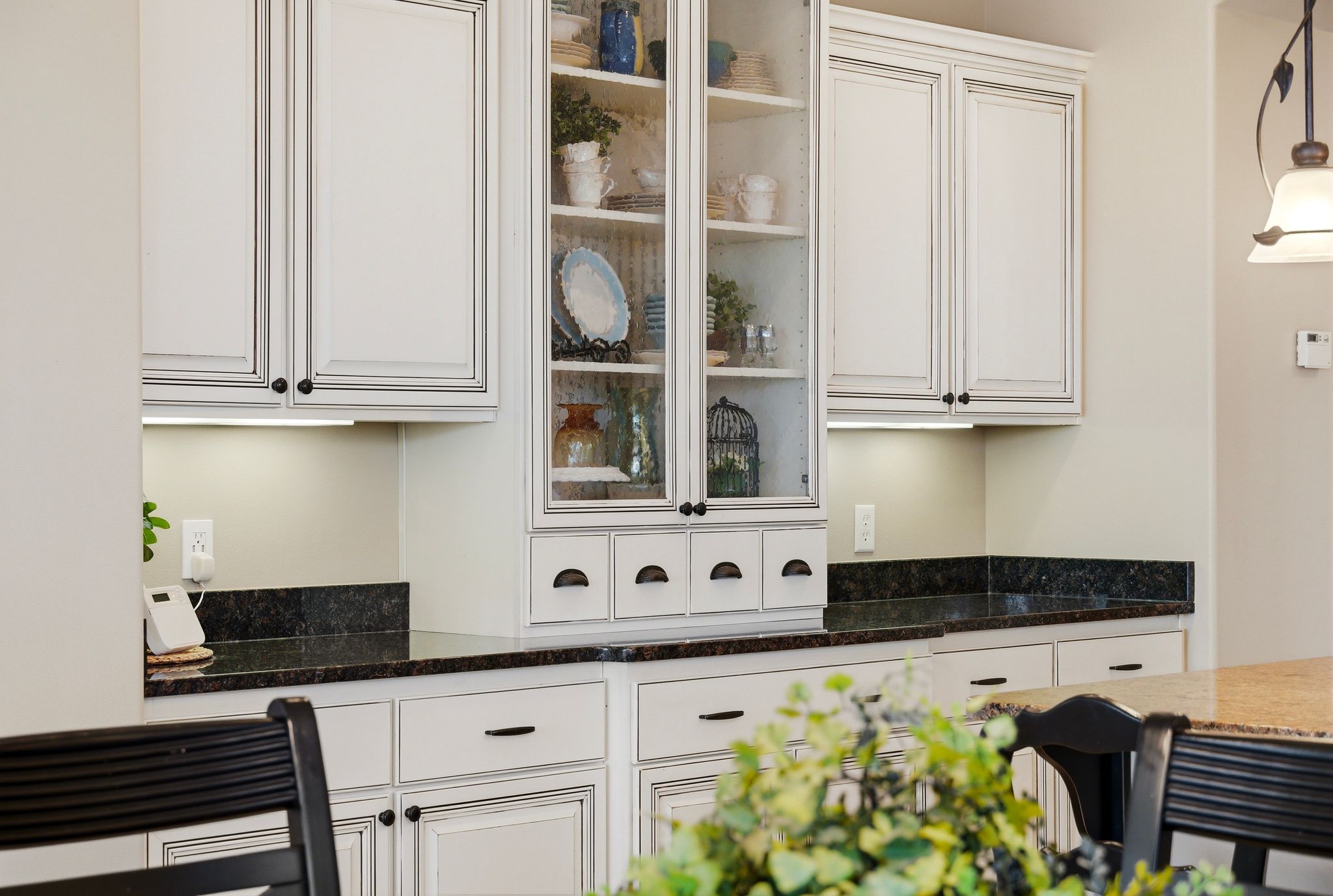 Kitchen with dark stone countertops, white cabinets, pendant lighting, and glass fronted cabinets