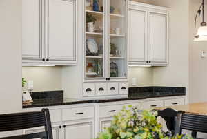 Kitchen with dark stone countertops, white cabinets, pendant lighting, and glass fronted cabinets