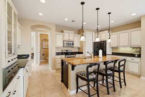 Kitchen featuring a kitchen bar, stainless steel appliances, dark stone countertops, a center island with sink, and glass insert cabinets