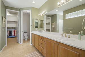 Full bath with a spacious closet, double vanity, light tile patterned flooring, and recessed lighting