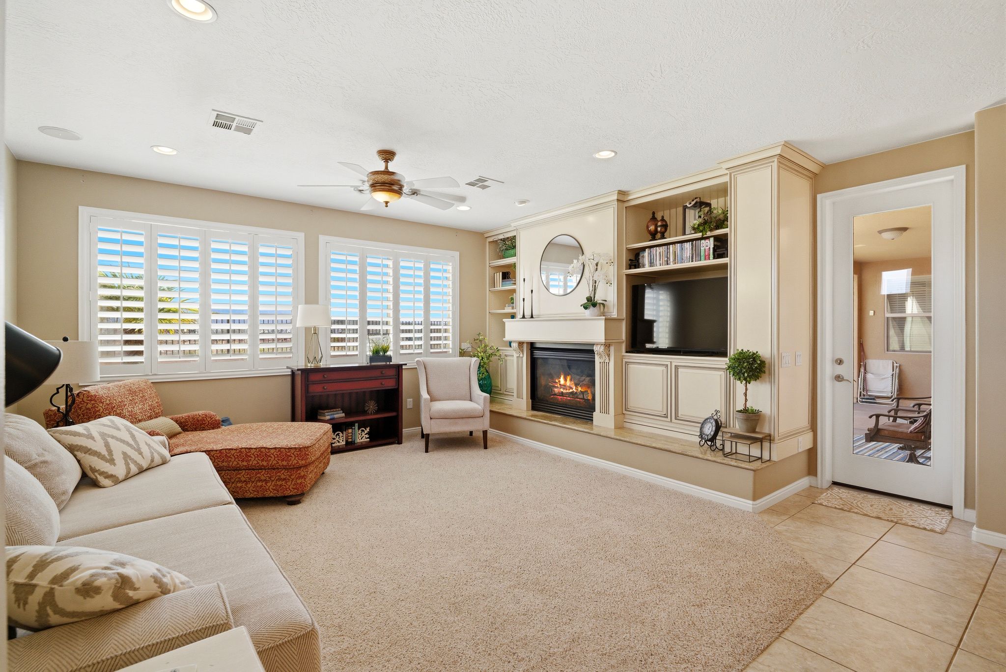 Living area with a glass covered fireplace, a ceiling fan, light tile patterned floors, light carpet, and built in features