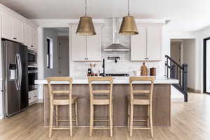 Kitchen featuring stainless steel appliances, a kitchen island with sink, white cabinets, decorative light fixtures, and light wood-style flooring