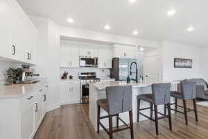 Kitchen featuring stainless steel appliances, a kitchen bar, a center island with sink, dark wood finished floors, and light stone counters