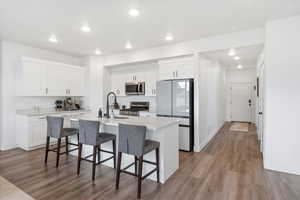 Kitchen featuring a kitchen bar, white cabinets, stainless steel appliances, recessed lighting, and light wood finished floors