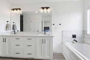 Ensuite bathroom featuring double vanity, light wood-type flooring, and a garden tub