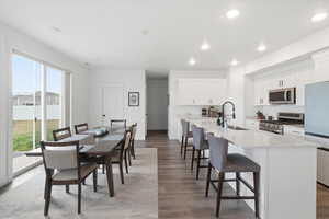 Kitchen with white cabinets, stainless steel appliances, a kitchen bar, light wood-style flooring, and light stone counters