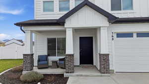Property entrance featuring board and batten siding, covered porch, a shingled roof, an attached garage, and stone siding