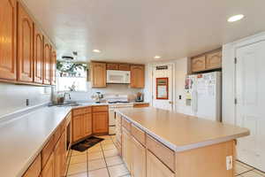 Kitchen with white appliances, light tile patterned floors, a kitchen island, light countertops, and recessed lighting