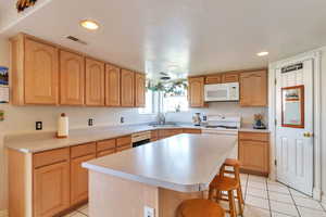 Kitchen featuring light countertops, white appliances, a breakfast bar area, light tile patterned flooring, and recessed lighting