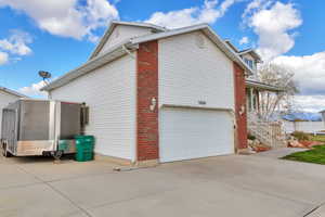 View of side of property featuring brick siding, driveway, covered porch, and an attached garage