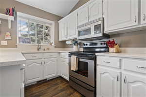 Kitchen with stainless steel appliances, white cabinets, light stone countertops, and lofted ceiling