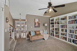 Living area featuring carpet flooring, lofted ceiling, ceiling fan, crown molding, and a chandelier