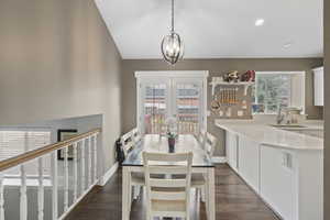 Dining room with dark wood-type flooring, hanging lights, and vaulted ceiling